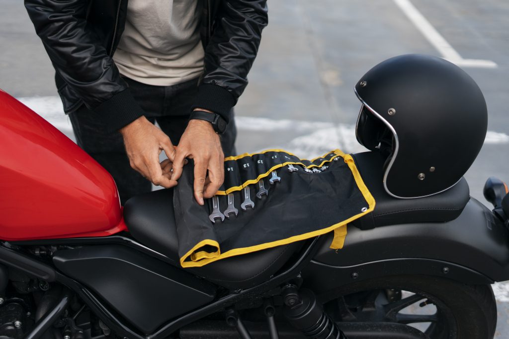 Image of a person's arms using tools resting on a black motorcycle seat.