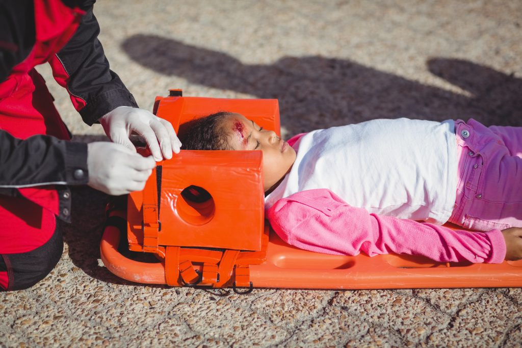 Image of an injured girl lying on a orange stretcher on the ground